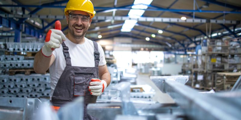 portrait-of-factory-worker-in-protective-equipment-holding-thumbs-up-in-production-hall